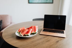sliced watermelon on a plate beside a laptop prepared for online therapy session 