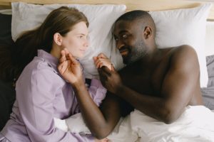 couple lying on bed while looking face to face discussing healthy boundaries they learned in therapy