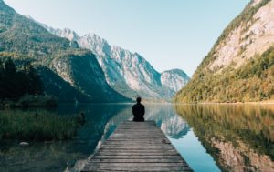 a person sitting on wooden planks across the lake scenery to decrease their anxiety 