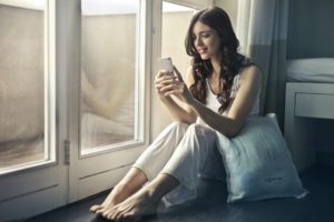 woman sitting beside window holding phone checking time for online therapy appointment in north Carolina 